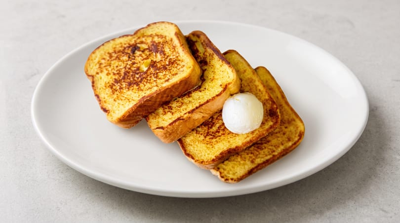 Four slices of golden French toast with a dollop of butter on a white plate.